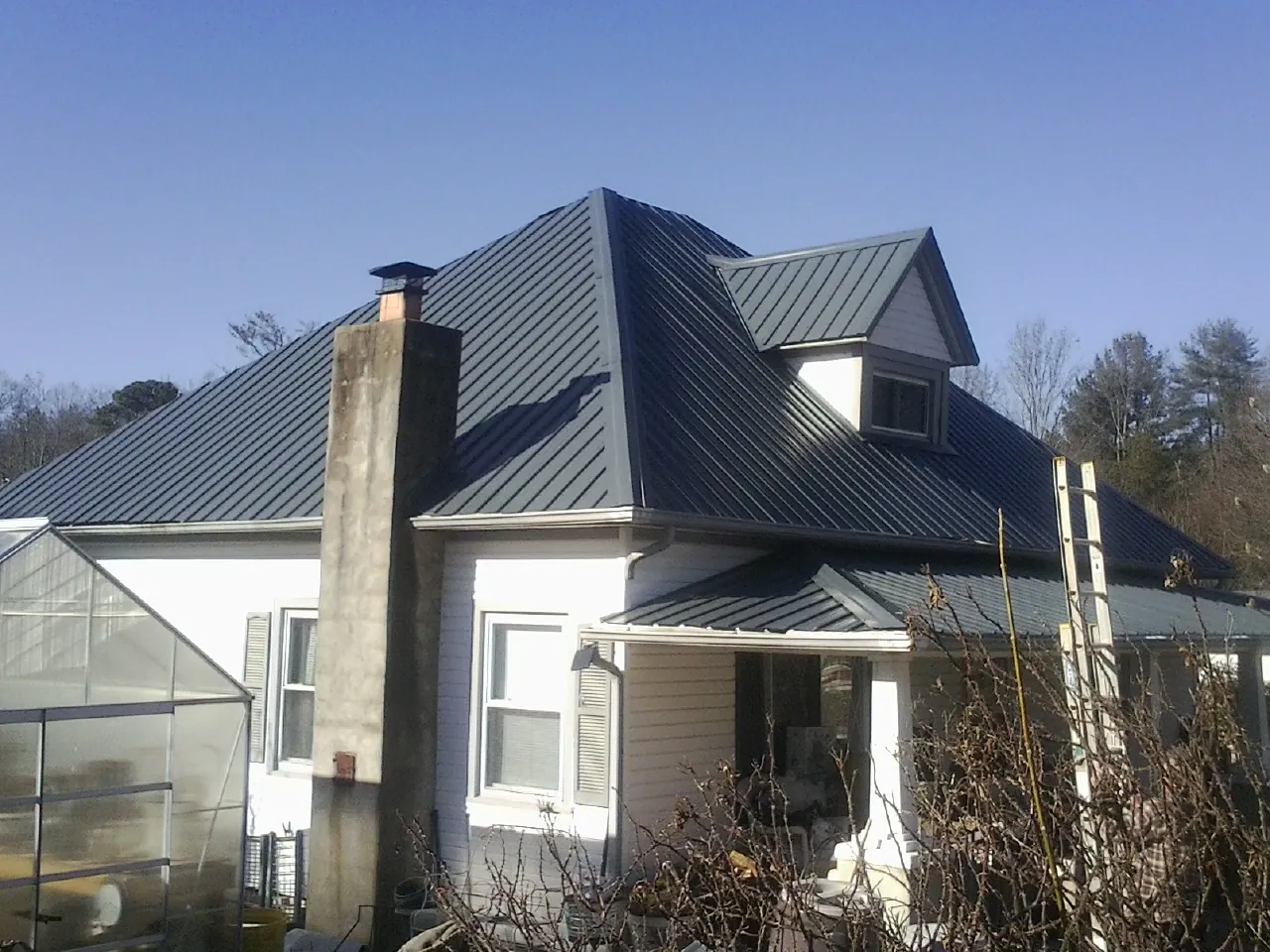 Dark blue standing seam metal roof on a white farmhouse with dormer — Slate & Tile Roof Repair by Roofing Brothers in Mc Allister
