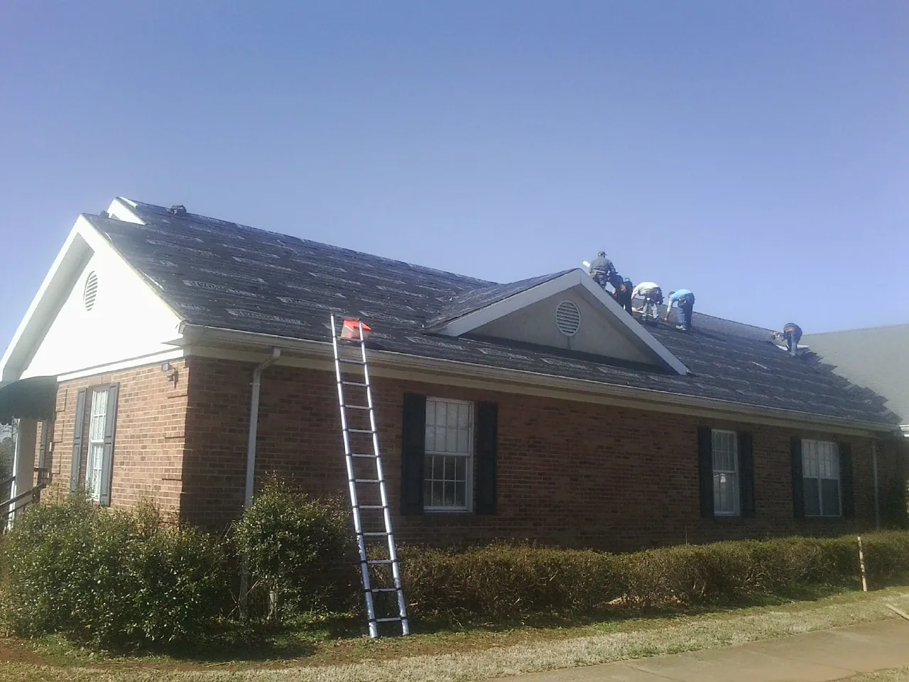Crew tearing shingles off a brick ranch roof with a ladder set — Emergency Roof Repair work by our crew in Mc Allister