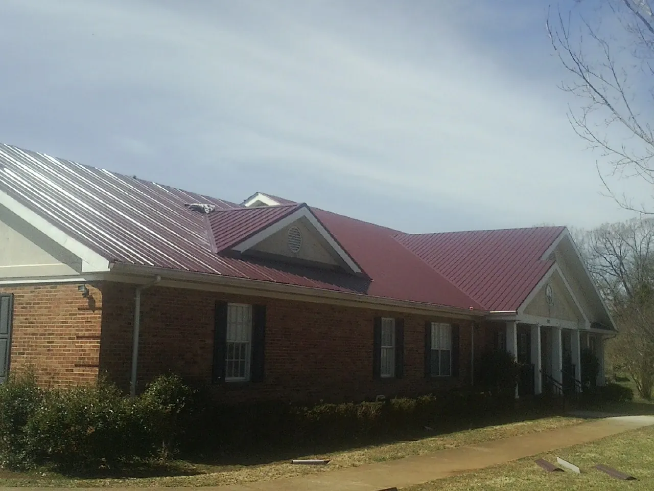 Red metal roof with gabled entries on a long brick building, from a Hail Damage Roof Repair job in Mc Allister