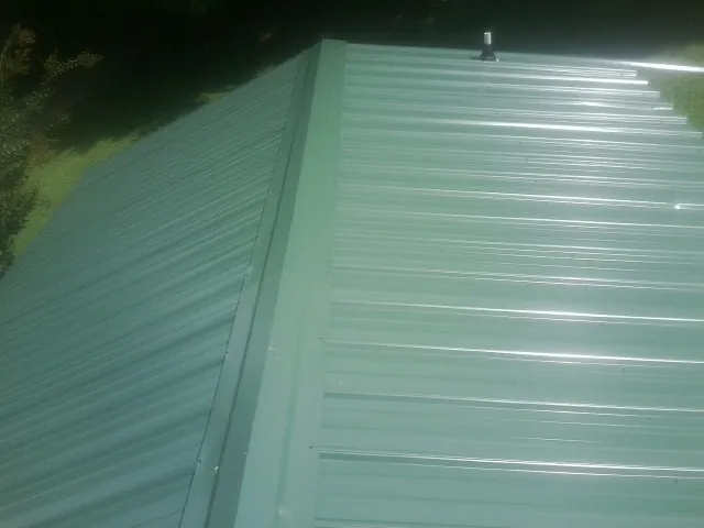 New green metal panels meeting at the ridge of a roof — Flat Roof Repair work by our crew in Mc Allister