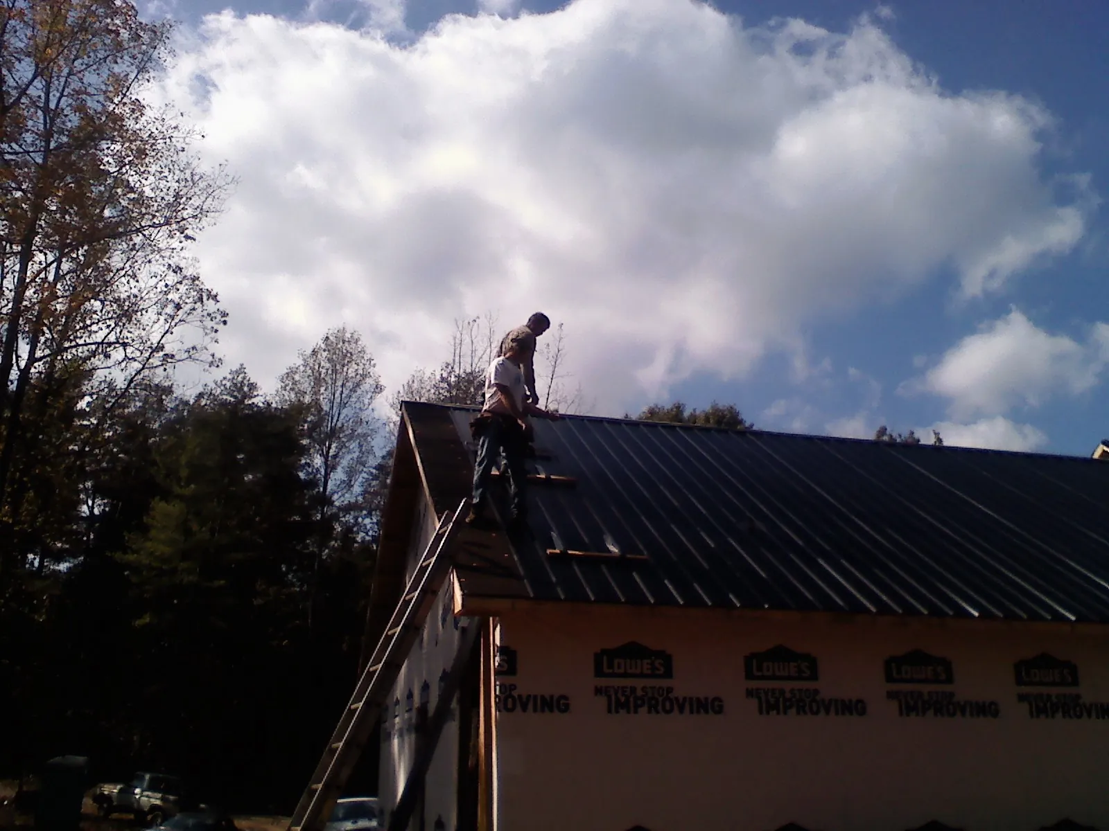 Roofer fastening dark metal panels high against a cloudy sky, from a Roof Inspection job in Mc Allister